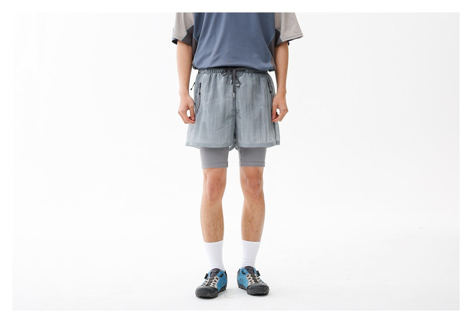 Front view of a person wearing light gray-blue running shorts over gray compression shorts against a white background.