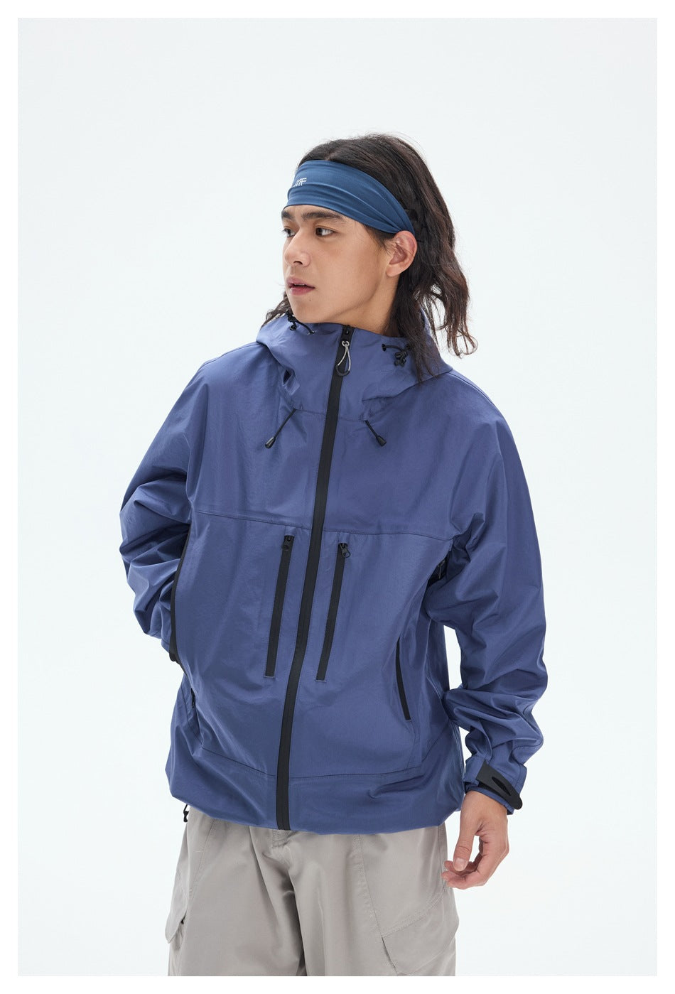 Angled view of a model wearing a blue hooded jacket with black zippers and drawcords.