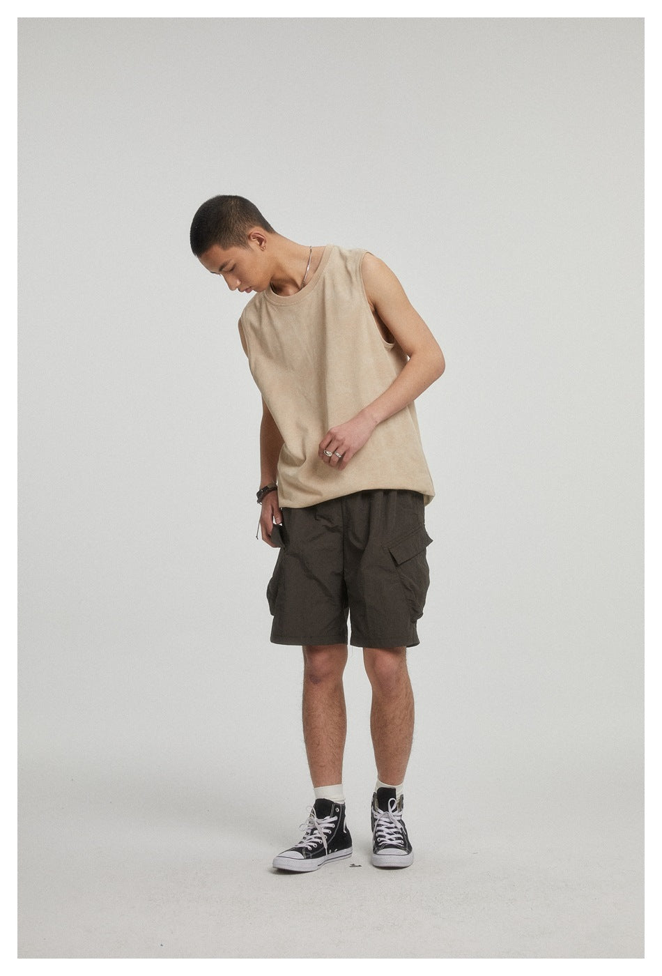 Model wearing a beige sleeveless top and dark cargo shorts, looking down in a studio.