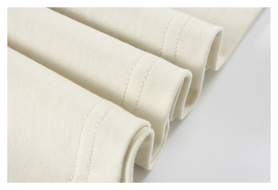 Close-up of three cream garment edges with stitched hems and softly rolled openings.
