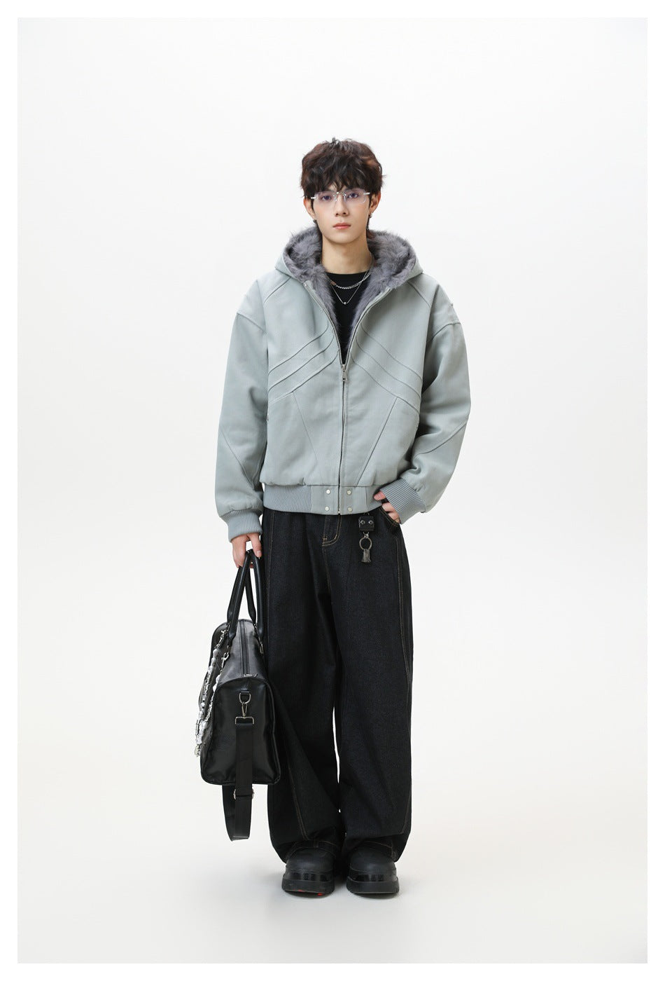 Full-length model wears a sage-gray hooded jacket with dark gray faux-fur lining, black jeans, and carries a black bag.