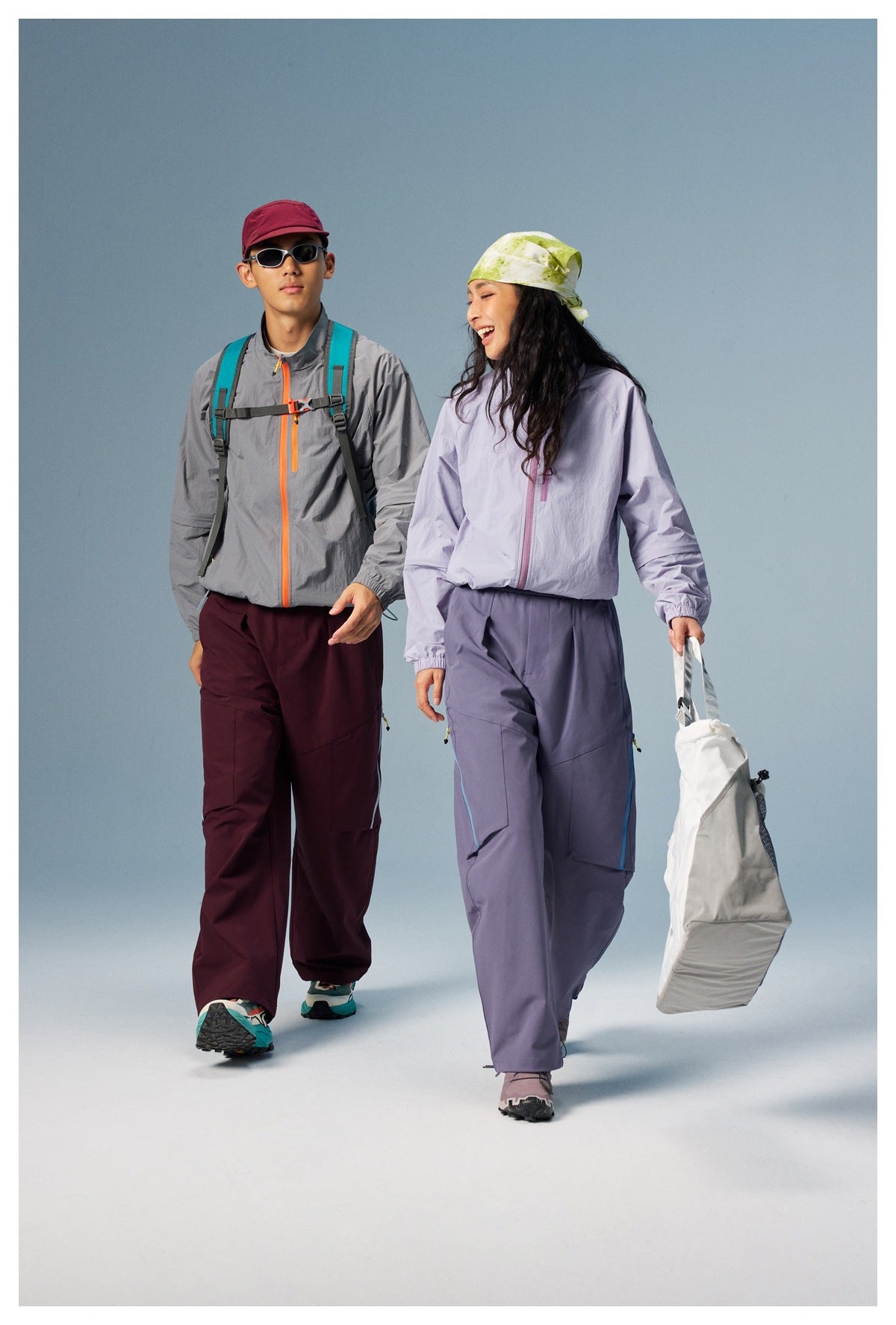 Two models walking in gray and light purple zip jackets with wide-leg pants and a white tote bag