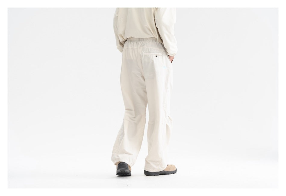 Rear view of a model wearing loose cream pants with an elastic waist and a small back pocket.