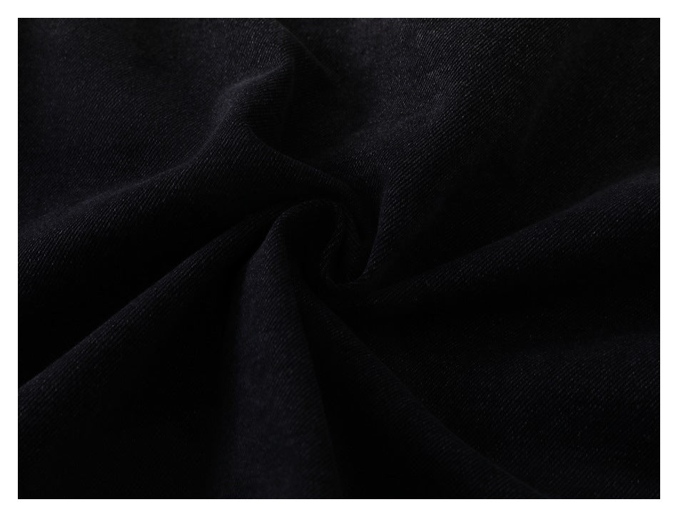 Close-up of dark black denim fabric gathered into folds, showing its diagonal weave.