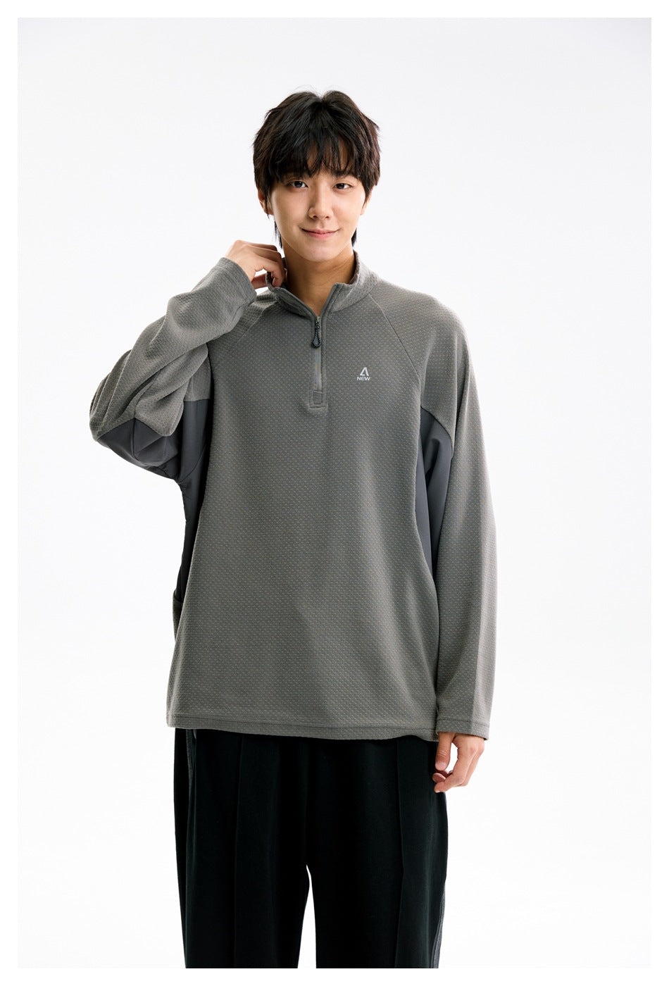 Model wearing a gray textured quarter-zip pullover with dark side panels and black pants, front view.