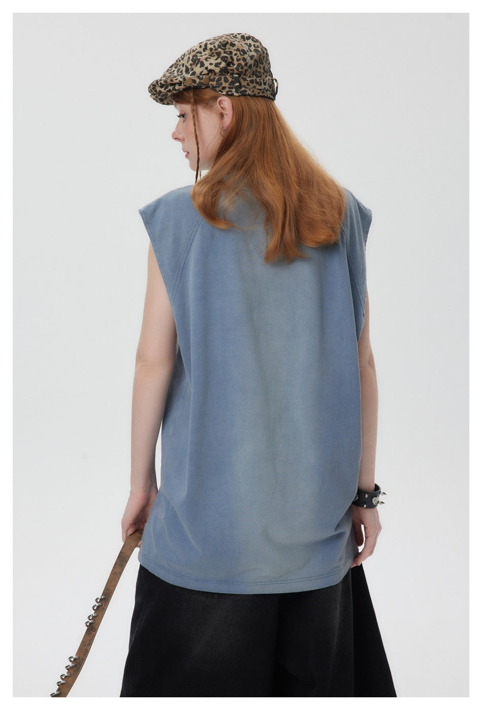 Angled rear view of a model wearing a faded blue sleeveless shirt with curved shoulder seams.