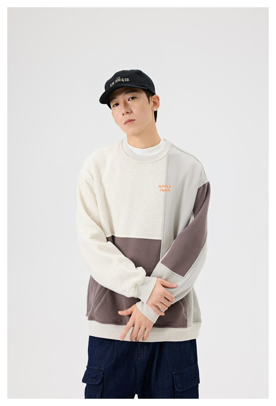 Model wearing an oatmeal, taupe and gray color-block crewneck sweatshirt with arms crossed, with cargo pants