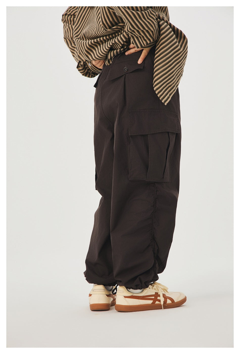 Cropped rear-side view of a person wearing dark brown cargo pants with a large flap pocket and gathered ankle cuffs.