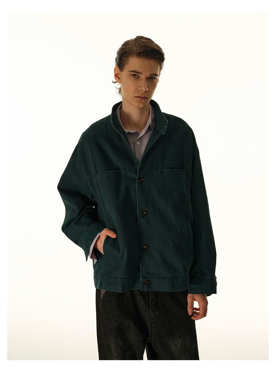 Model wearing an oversized dark teal button-front jacket with a raised collar and large front pockets.