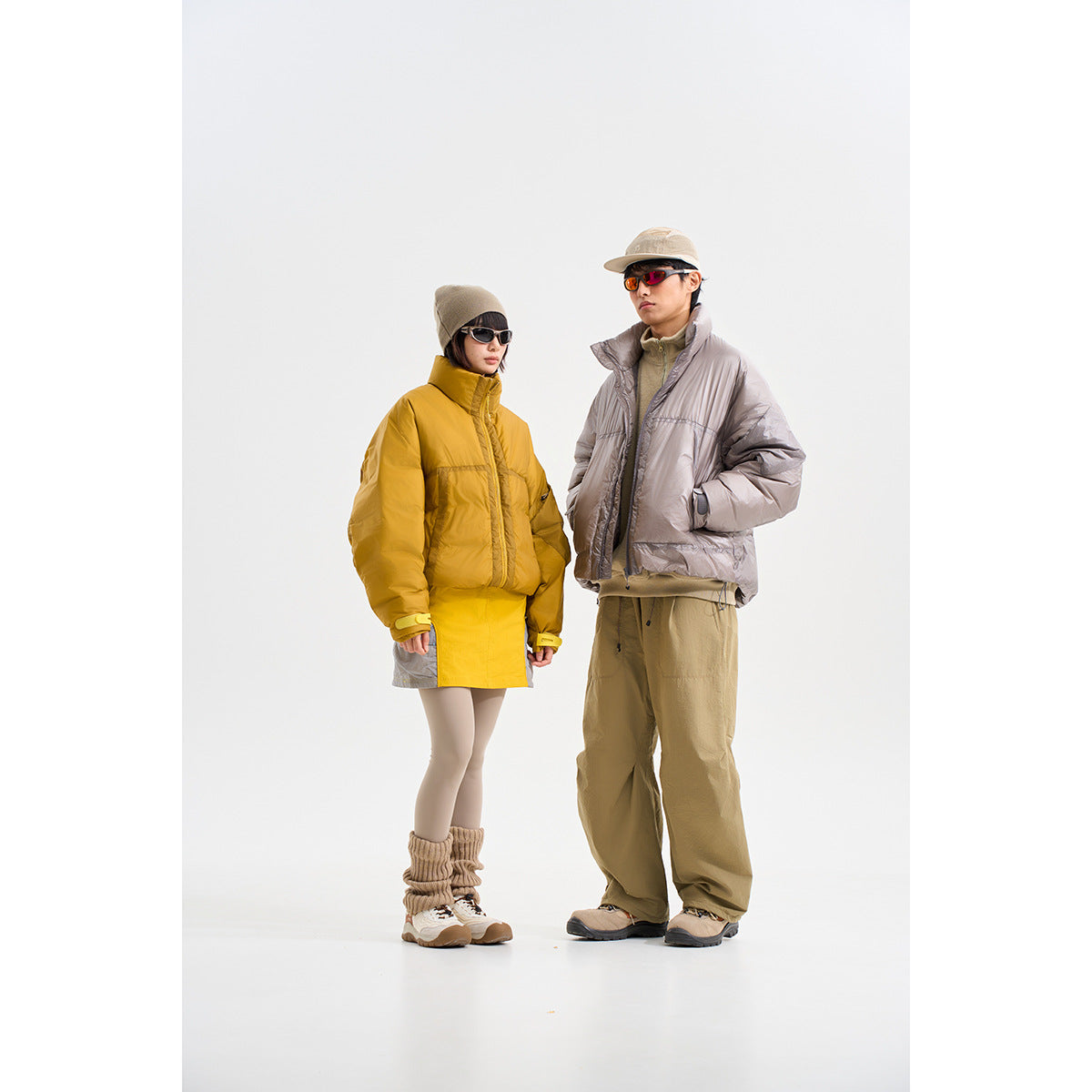 Two models wearing puffer jackets: one mustard yellow and one light gray, with neutral outdoor-inspired outfits.