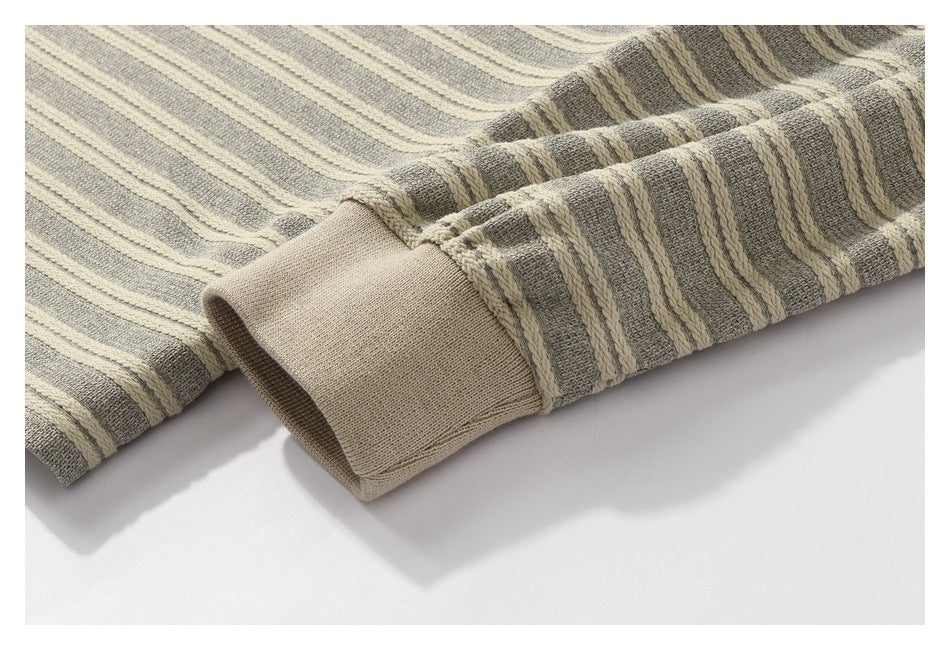 Close-up of a plain beige ribbed cuff beside the garment's gray and cream striped knit sleeve.