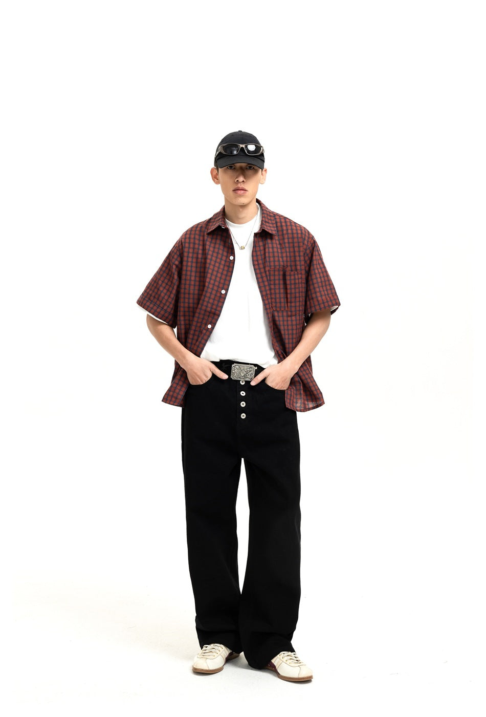 Model wearing black wide-leg button-fly jeans with a plaid short-sleeve shirt, white tee and cap, front view