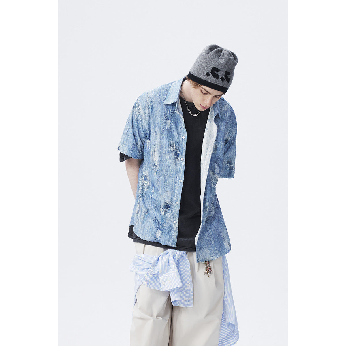 Model in a blue distressed-pattern short-sleeve button-up over a black tee, with a gray beanie and striped shirt tied at the