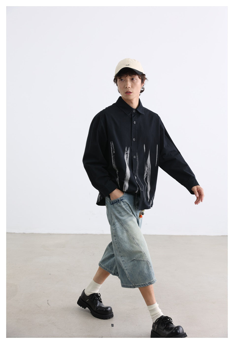 Full-length view of a model wearing a black shirt with white brushstroke graphics and light denim shorts.