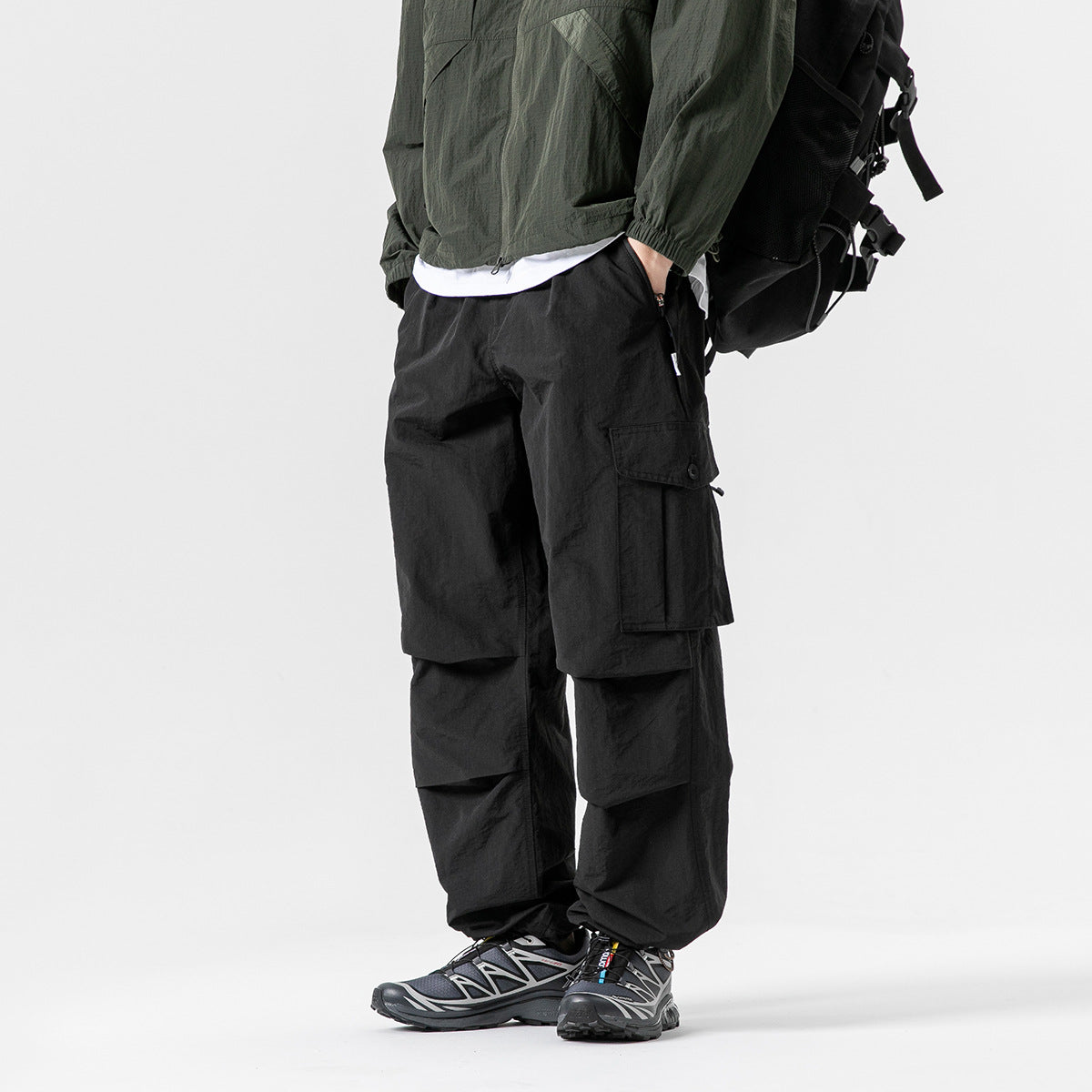 Cropped model wearing black cargo pants with layered knee panels and large flap pockets, paired with a dark jacket.