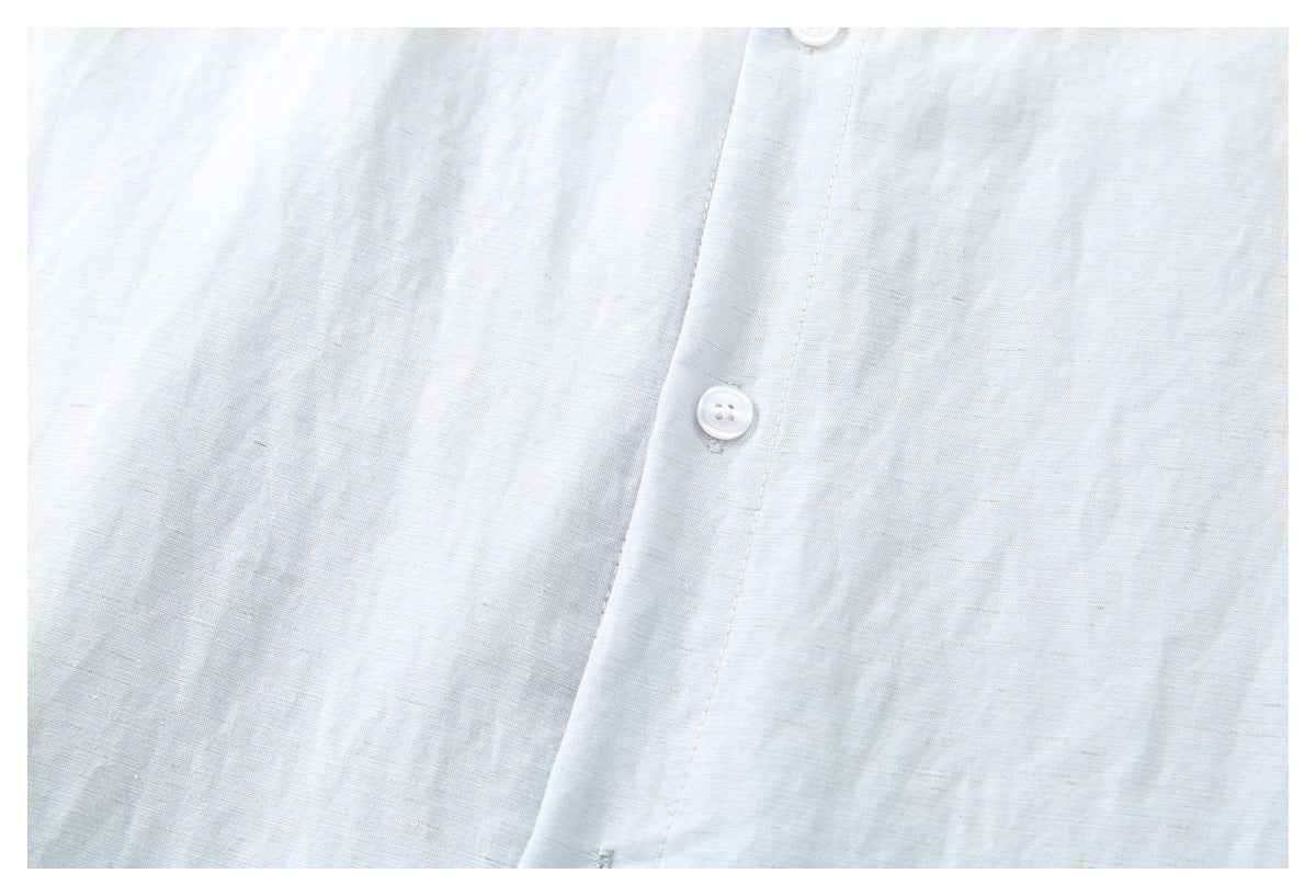 Close-up of a pale blue-gray shirt front with a white button and stitched placket.