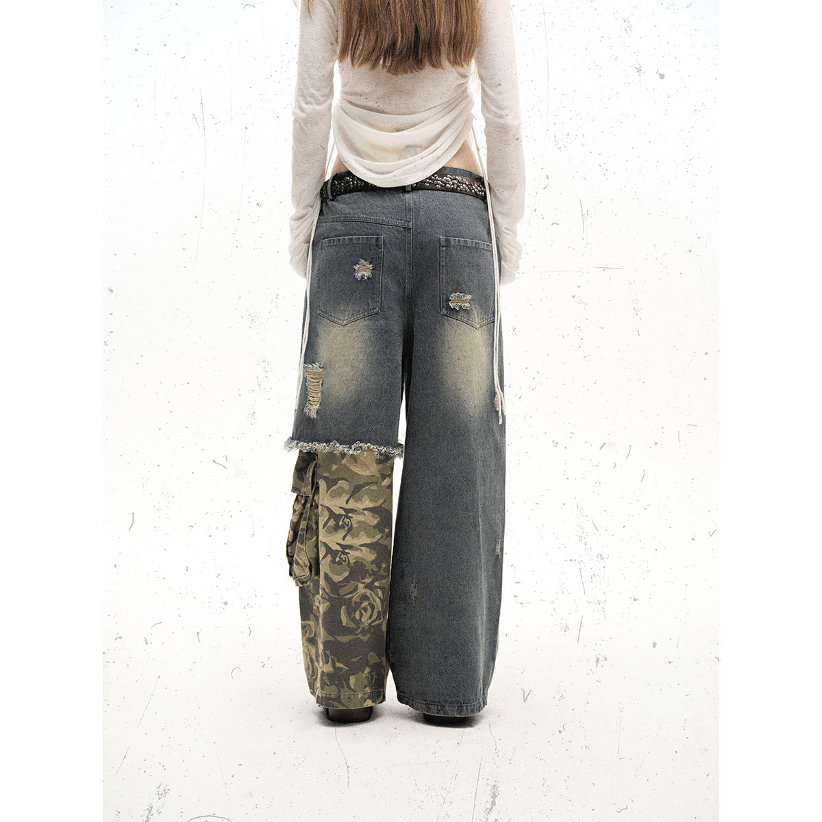 Back view of a model wearing oversized gray jeans with distressed pockets and one olive camouflage cargo leg.