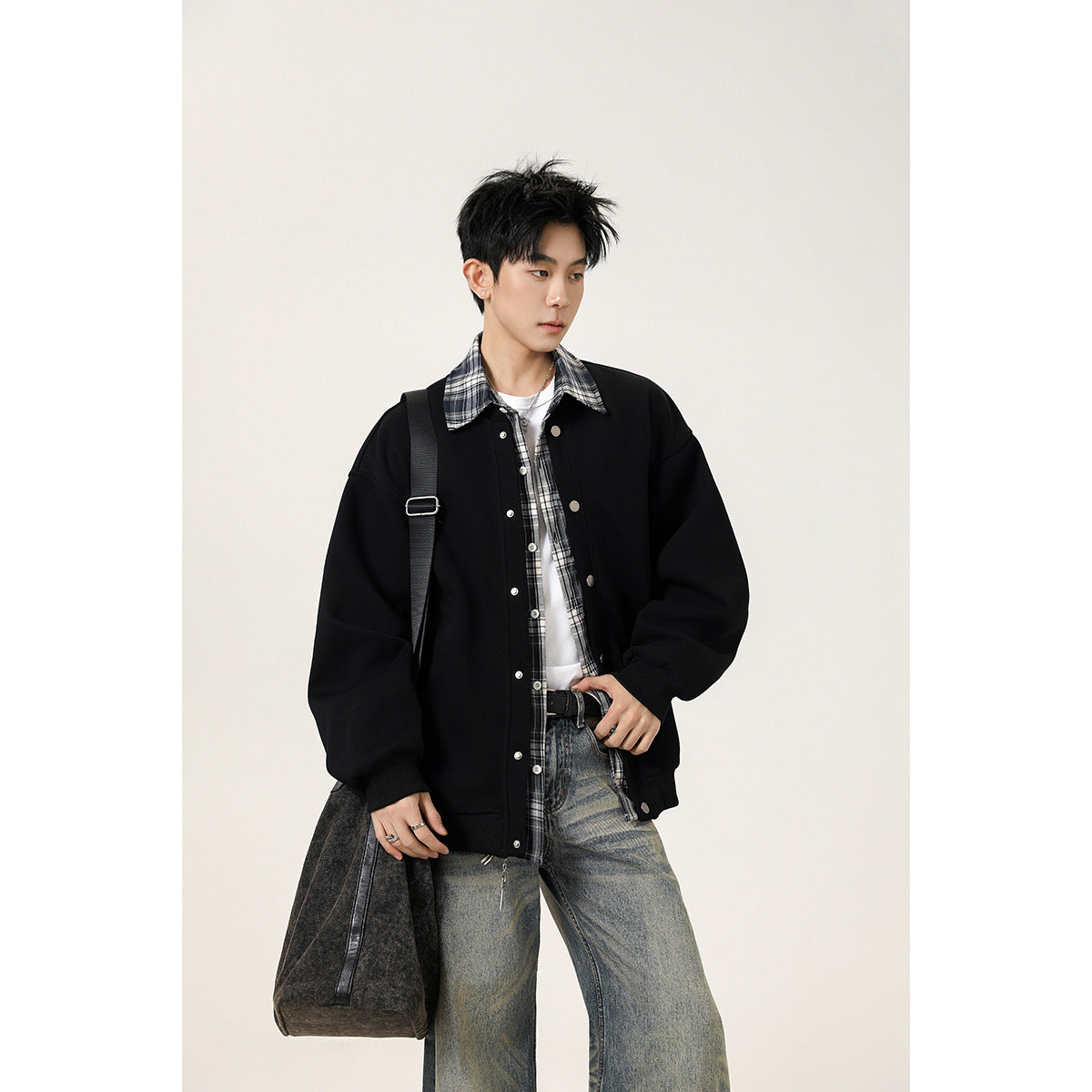 Model wearing an oversized black snap-front jacket with a black-and-white plaid shirt.