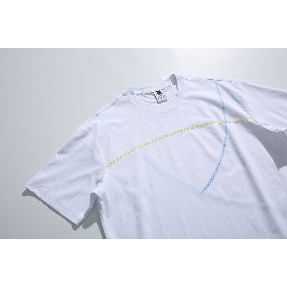 Angled close view of a white short-sleeve T-shirt with curved lime and blue seam details.