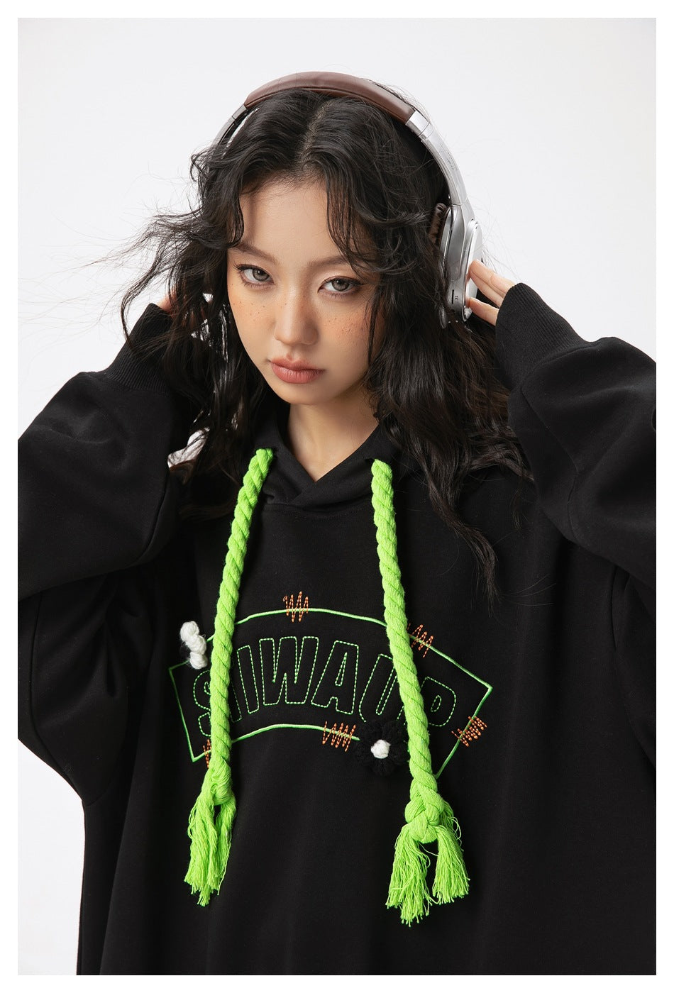 Close-up of a model wearing a black hoodie with neon green braided drawstrings and outlined chest lettering.