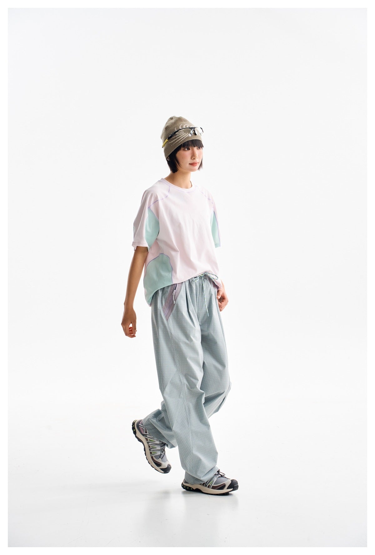 Model wearing loose sage-check trousers and a white pastel-panel T-shirt, shown in a three-quarter pose.