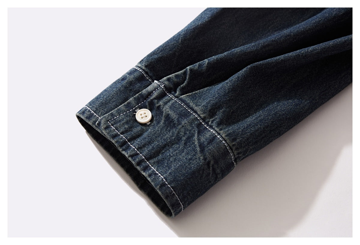 Close-up of a dark indigo denim shirt cuff with white stitching and a small white button.