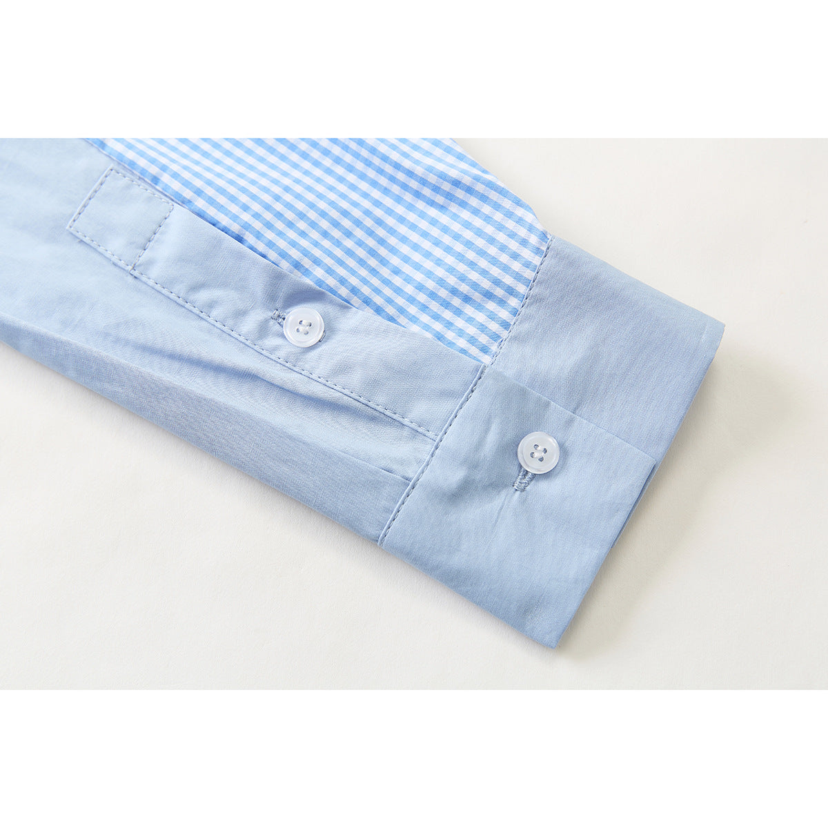 Close-up of a light blue shirt cuff with white buttons and blue-and-white gingham fabric above it.