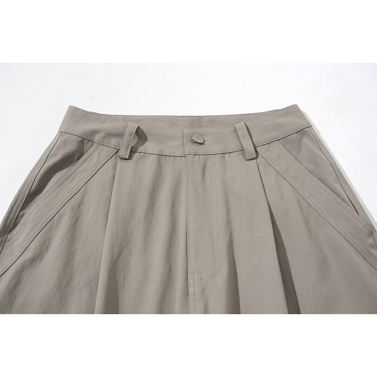 Close-up of taupe cargo pants showing the buttoned waistband, belt loops, pleats and angled front pockets.
