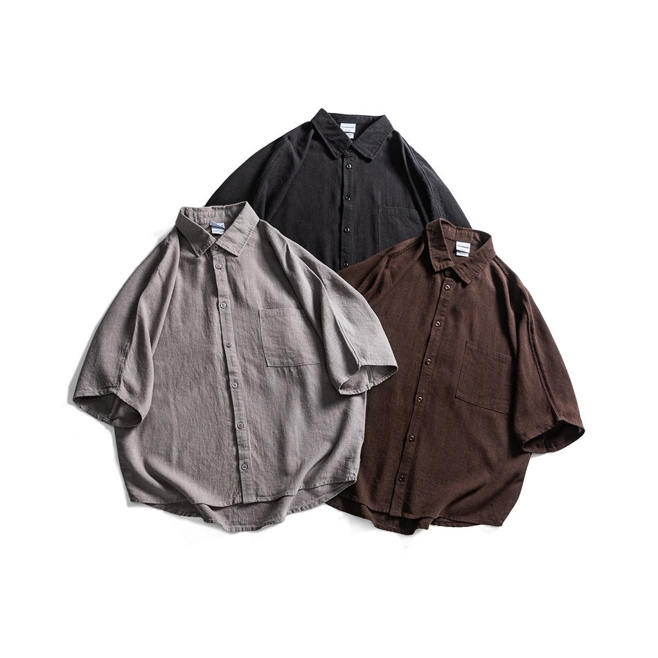 Three short-sleeve button-up shirts with chest pockets, arranged in gray, dark brown, and black.