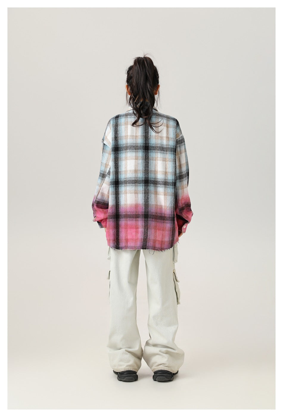 Back view of a model wearing an oversized blue-gray and pink plaid shirt with light cargo pants.
