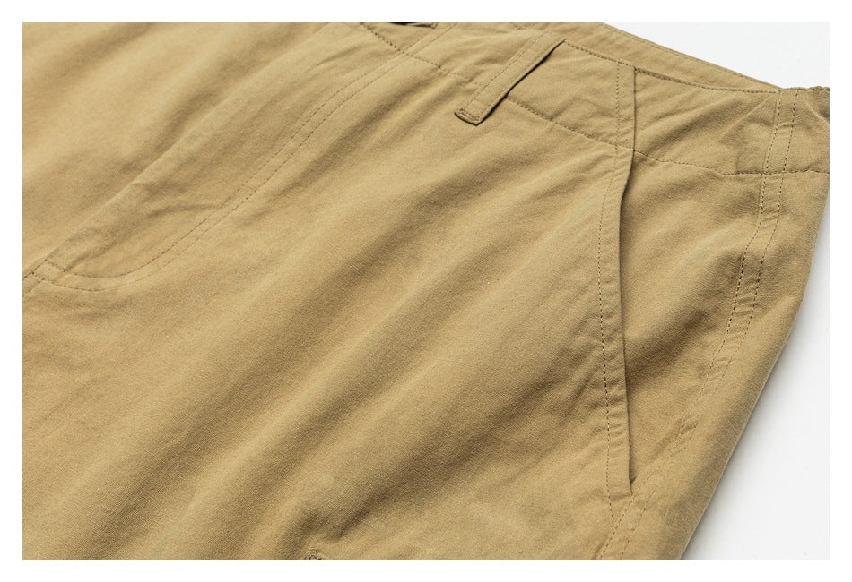 Close-up of tan trousers showing a curved front pocket, belt loop, and side seam.
