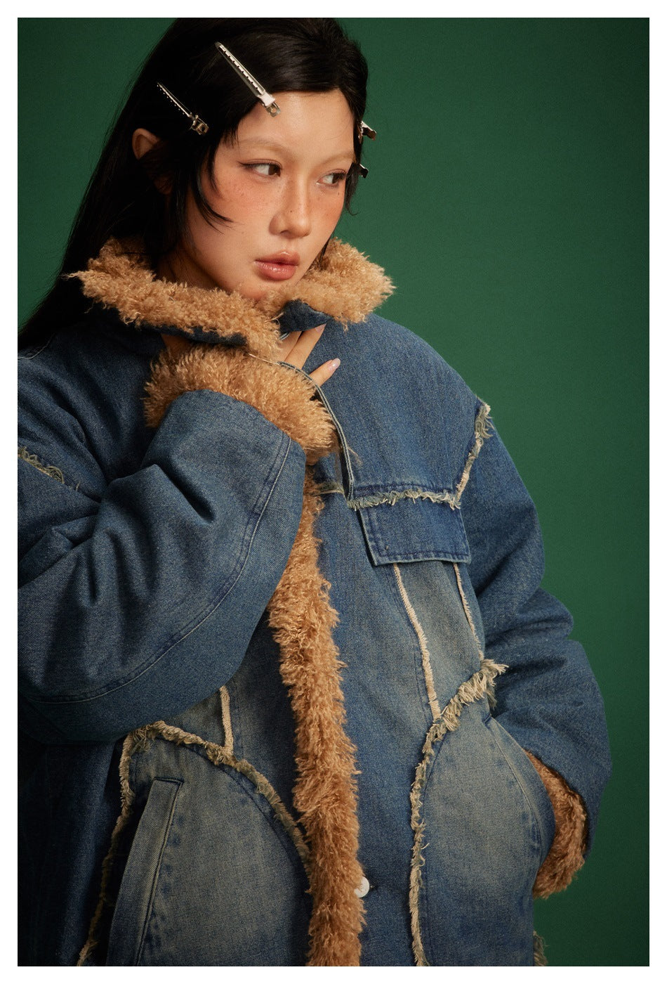 Model wearing a blue denim jacket with tan curly lining and raw-edged panels, shown from the front against a green backdrop.