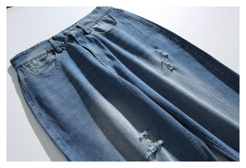 Angled flat lay of blue distressed jeans, showing the front pockets, fly, and ripped patches.