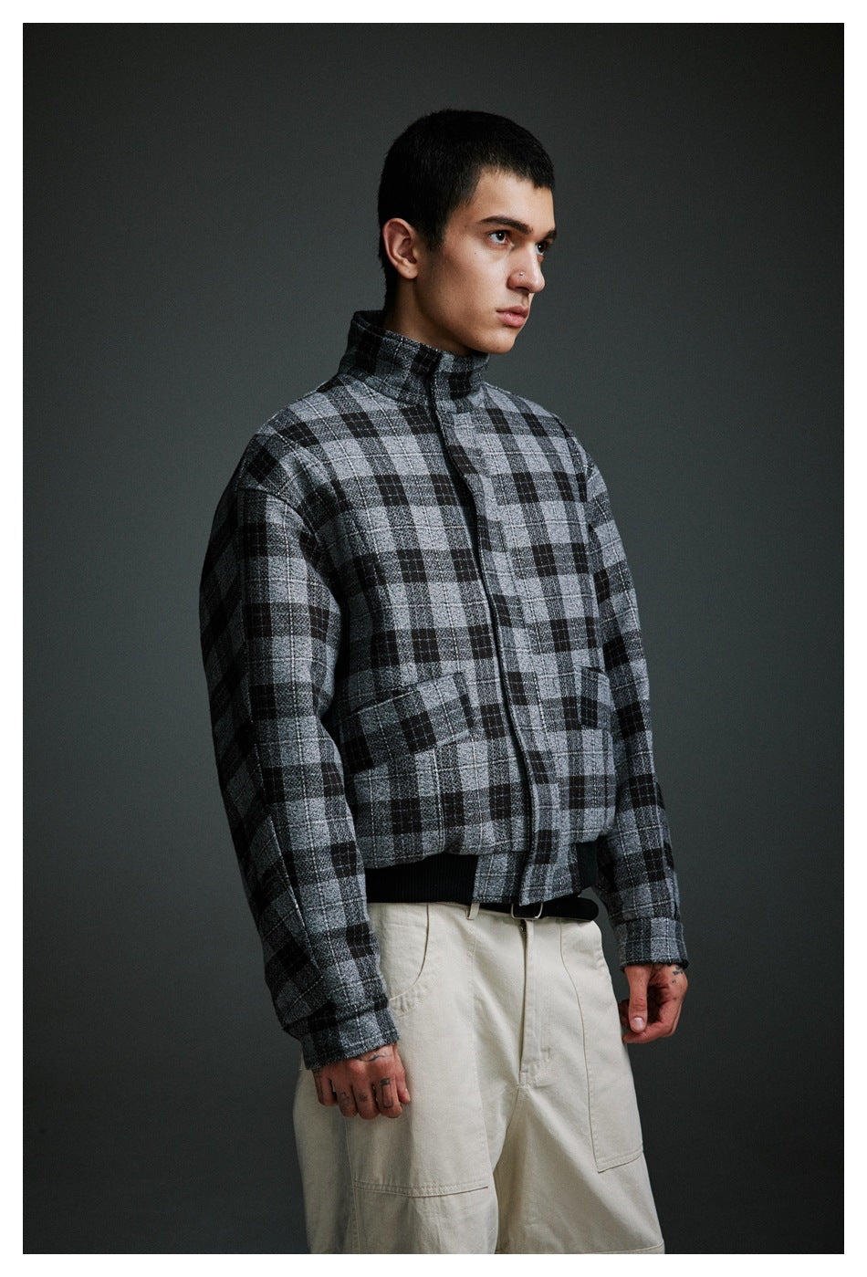 Man in a gray and black plaid high-collar jacket, shown at an angle with cream cargo pants.