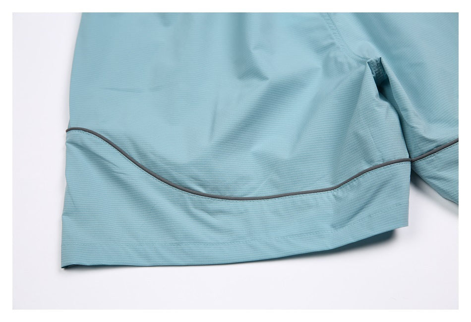 Close-up of pale aqua garment hem with curved dark piping and fine pinstripes.