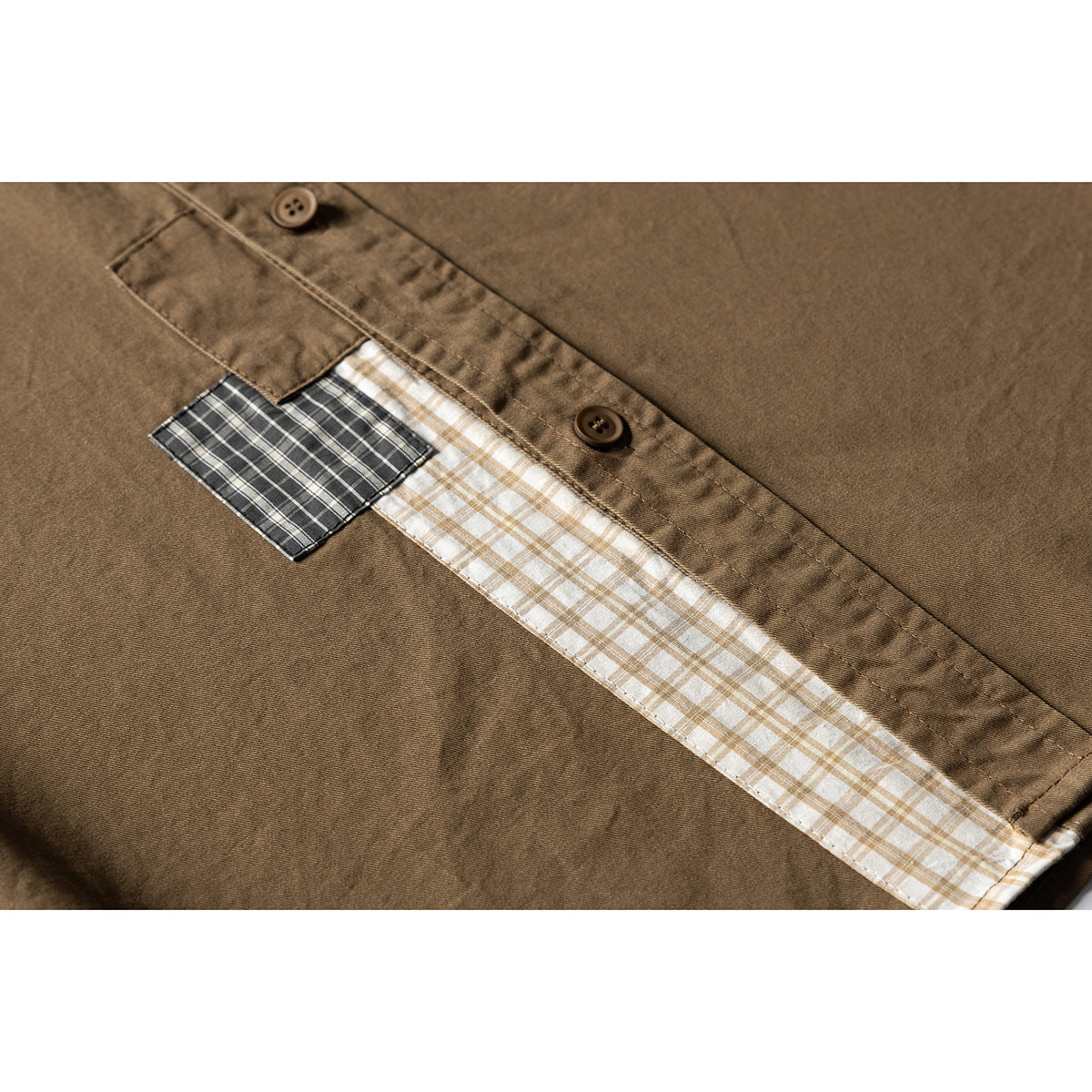 Close-up of a brown shirt placket with buttons and contrasting plaid fabric inserts.