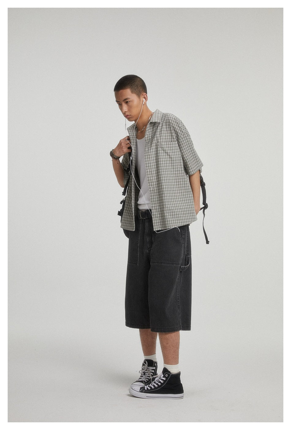 Model wearing a gray checked short-sleeve shirt over a white tank with loose black knee-length shorts.