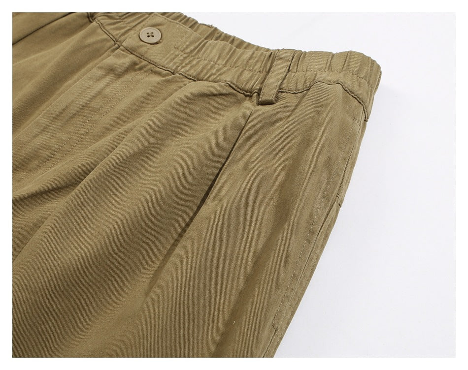 Close-up of khaki trousers showing the elastic waistband, button, belt loop and front pleats.
