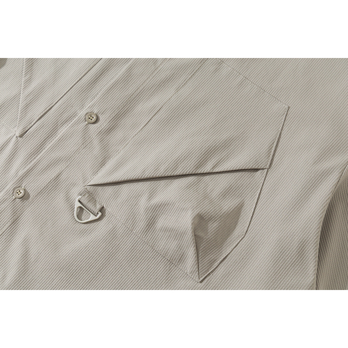 Close-up of the light gray shirt’s angular chest pocket, button, and small metal loop detail.