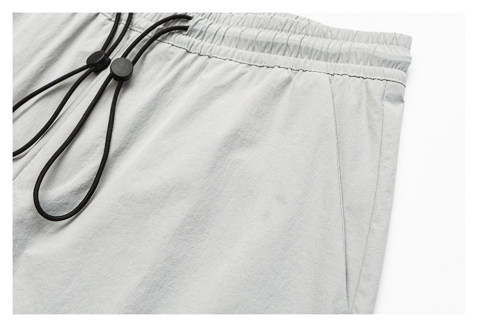 Close-up of light gray pants showing the elastic waistband, black drawcords, and side pocket seam.