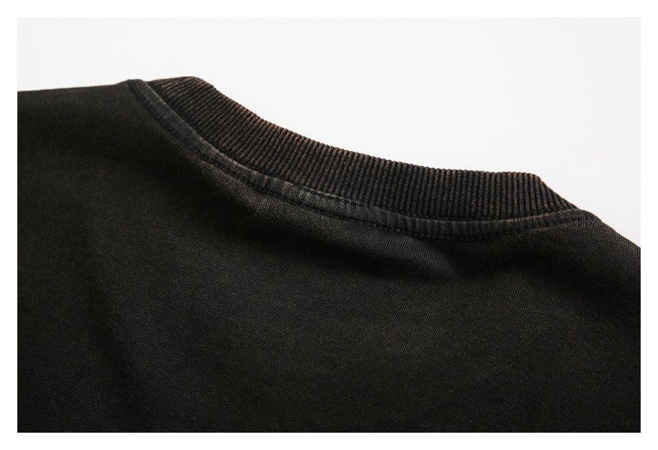 Close-up of a black garment's ribbed crew neckline and shoulder seam.