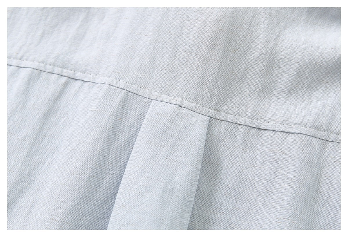 Close-up of a stitched back yoke and pleat on a pale blue-gray shirt.