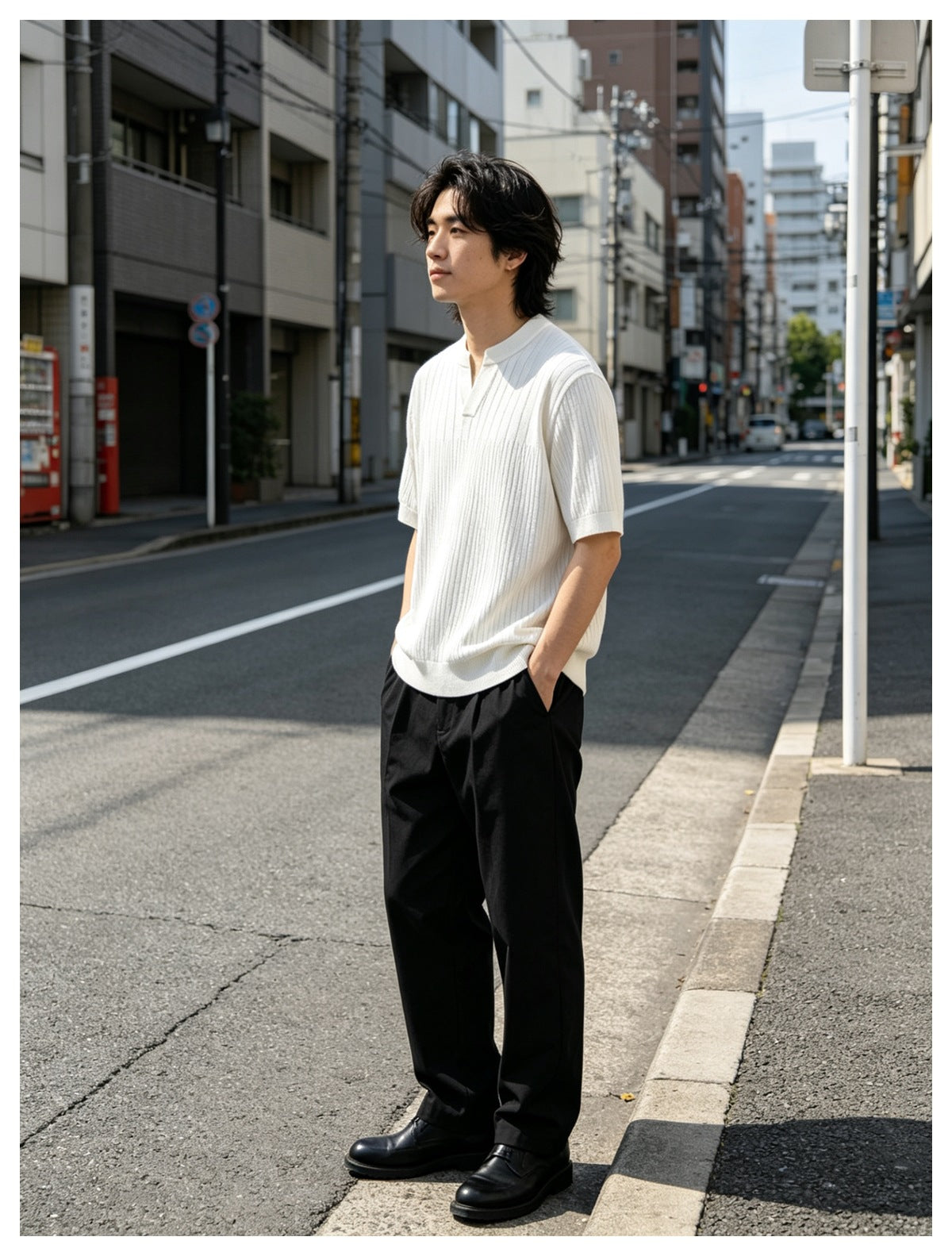 Man standing on a city street wearing a white ribbed knit short-sleeve top with black trousers and black shoes