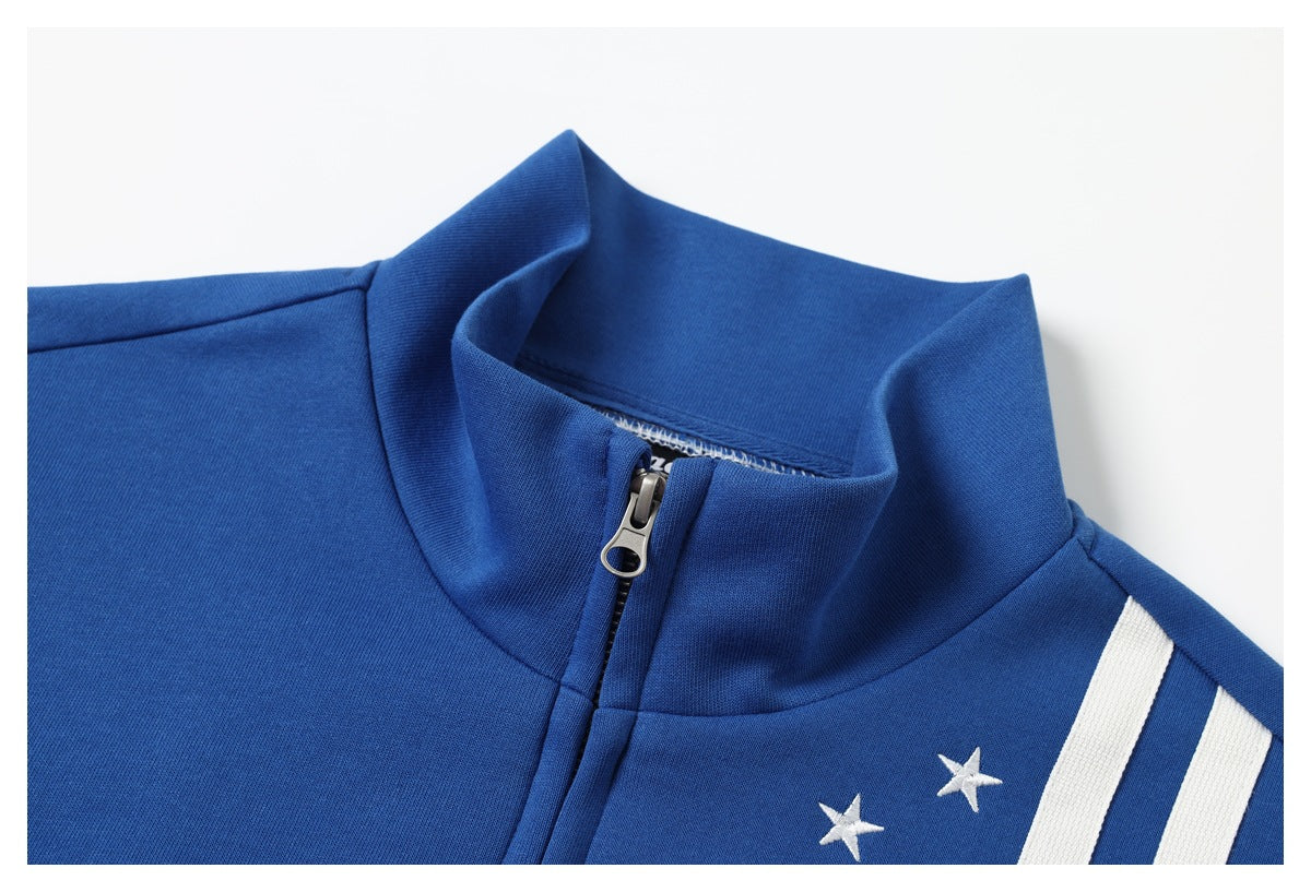 Close-up of a blue track jacket’s stand collar, zipper, white star embroidery, and shoulder stripes.