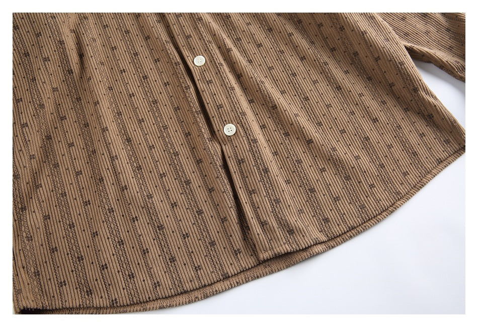 Close view of the lower front and curved hem of the tan patterned button-up shirt.