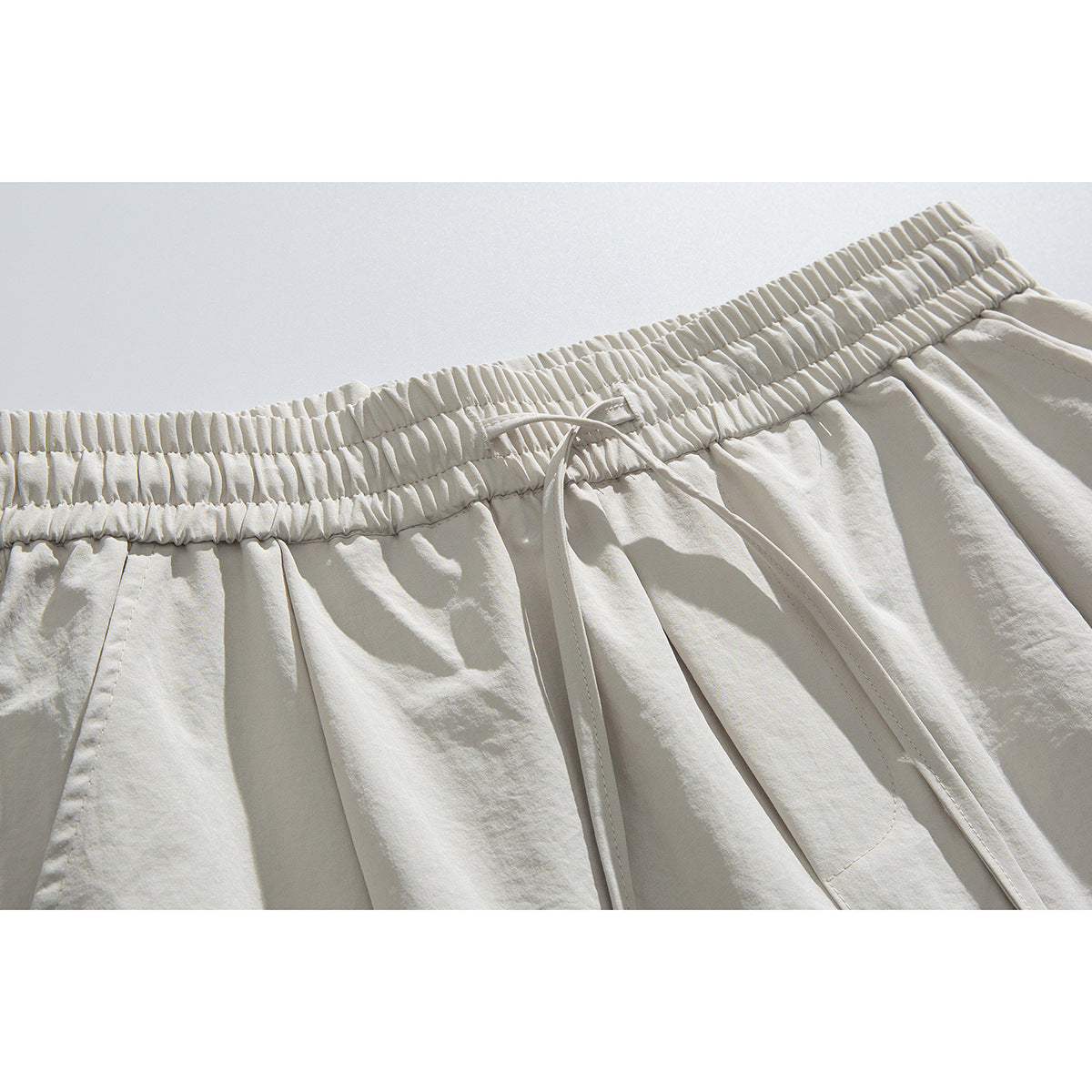 Close-up of cream pants showing the gathered elastic waistband, drawstring, and front pleats.