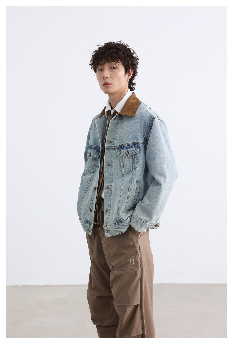 Full-length view of a model in a light-wash denim jacket with a brown collar and loose brown trousers.