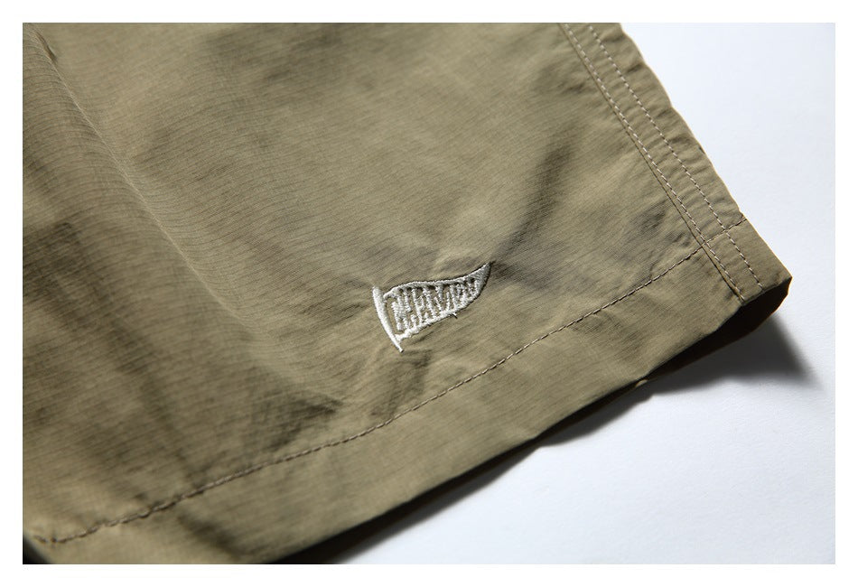 Close-up of a small white embroidered emblem and double-stitched hem on olive-khaki shorts.