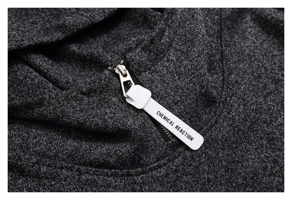 Close-up of a dark heather-gray garment zipper with a white pull tab printed “CHEMICAL REACTION.”
