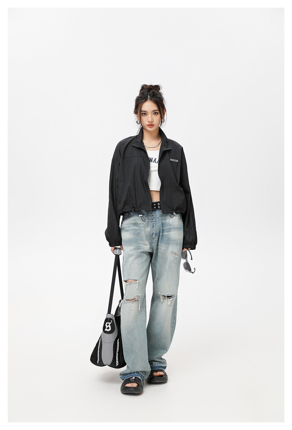 Model wearing a black cropped zip jacket with a stand collar and drawstring hem, paired with distressed light-wash jeans.